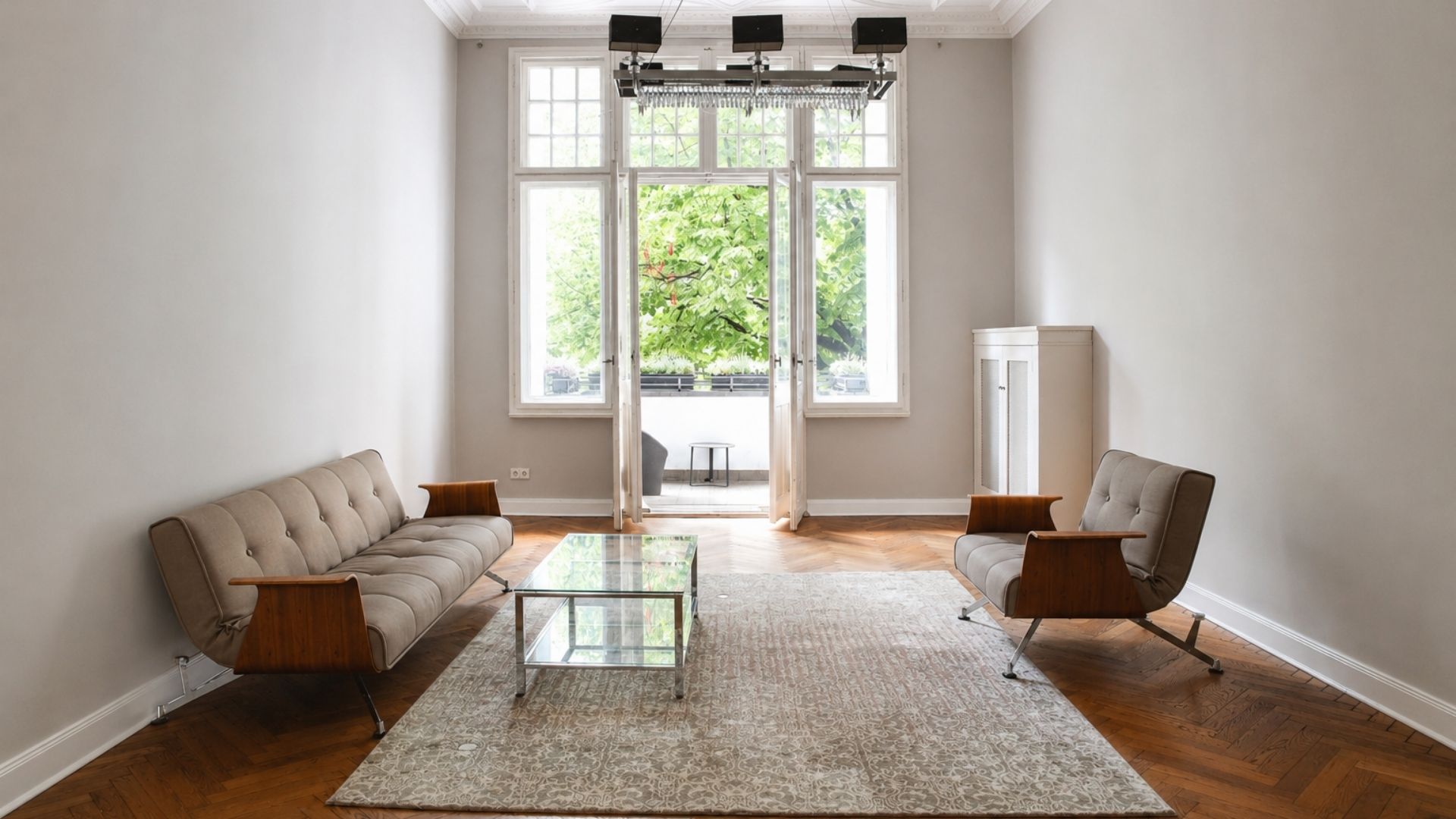 Heller Altbauraum von Beyond & Bloom mit hohen Fenstern, Balkonblick, Parkettboden, Teppich, Sofa, Sessel und Glastisch.