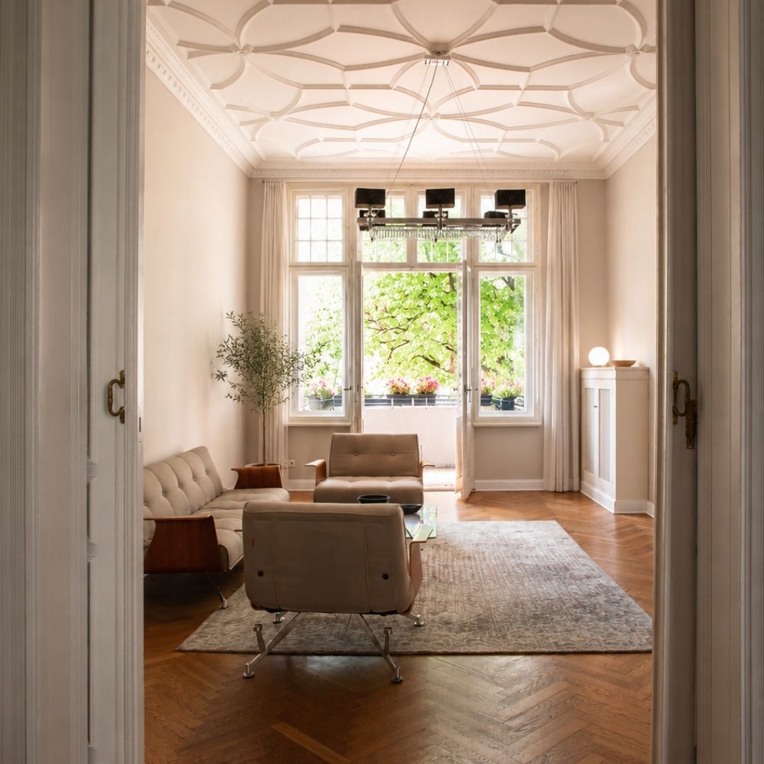 Lounge-Bereich von Beyond & Bloom mit Altbaudecke, hohen Fenstern, Balkonblick, Parkettboden, Teppich und hellen Sitzmöbeln.
